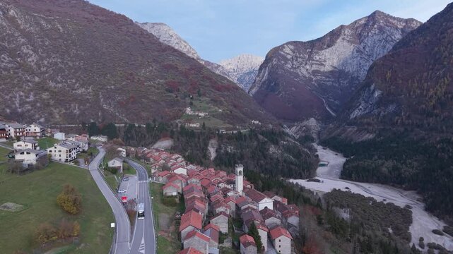 Aerial view of a village with red-roofed houses nestled in a deep valley surrounded by steep mountains and a winding road in Pordenone, Friuli-Venezia Giulia, Italy.