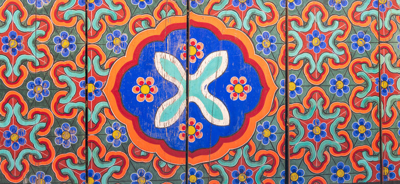 Close-up of vibrant traditional dancheong floral patterns painted on wooden ceiling beam of Buddhist temple in South Korea.