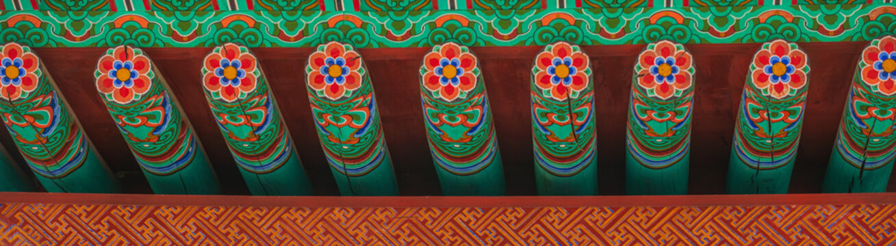 Traditional colorful dancheong lotus patterns on wooden rafters and decorative eaves of a Buddhist temple pavilion in South Korea.