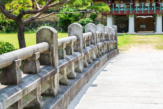 Perspective view of traditional stone bridge railing leading toward wooden temple pavilion on sunny day in South Korea.