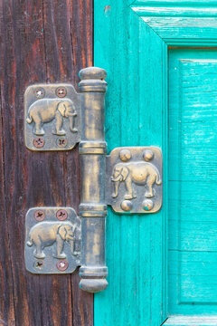Close-up of vintage bronze door hinge engraved with elephant figures on cyan painted wooden temple door in South Korea.