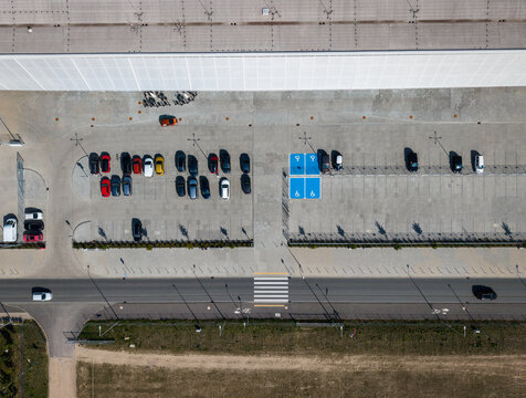 Aerial view of a parking lot featuring blue accessible parking spaces, rows of parked cars, and a nearby road with a crosswalk in Opole, Opole Voivodeship, Poland.