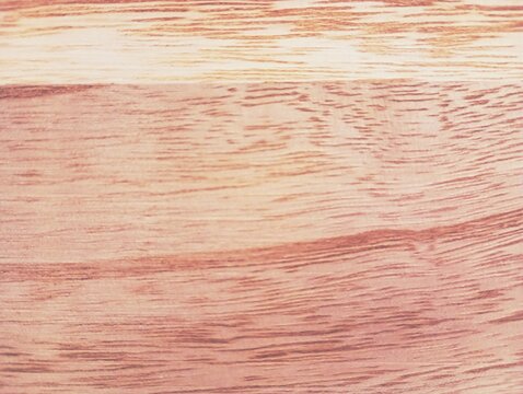 A detailed macro texture of a smooth polished wooden board, showcasing natural organic wood grain lines, parallel soft fibers, and a light pinkish brown timber surface color.