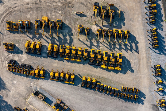 Aerial view of rows of yellow construction excavators parked in a large dirt lot with long shadows in LaGrange, New York, United States.