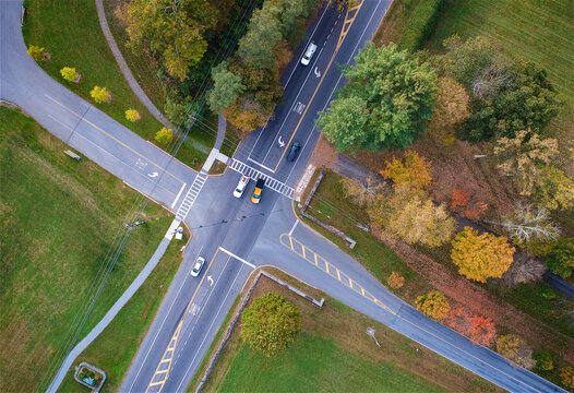Aerial view of a road intersection surrounded by autumn trees and green fields with cars driving on the asphalt roads in Hyde Park, New York, United States.