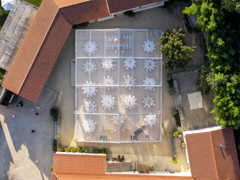 Aerial view of a transparent marquee tent set up for an outdoor event with round tables and chairs, surrounded by historic buildings with terracotta roofs in Giao, Porto, Portugal.