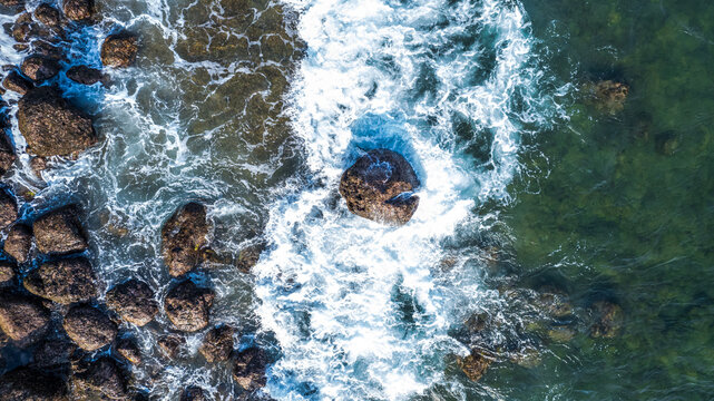 Aerial view of ocean waves crashing against dark rocks along the coastline in Bajawa, Nusa Tenggara Timur, Indonesia.