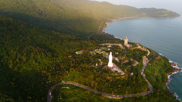 Aerial view of the Linh Ung Pagoda featuring the giant Lady Buddha statue surrounded by lush green forests and coastal roads overlooking the sea in Da Nang, Vietnam.