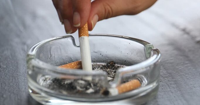 Woman putting out in ashtray at black table, closeup