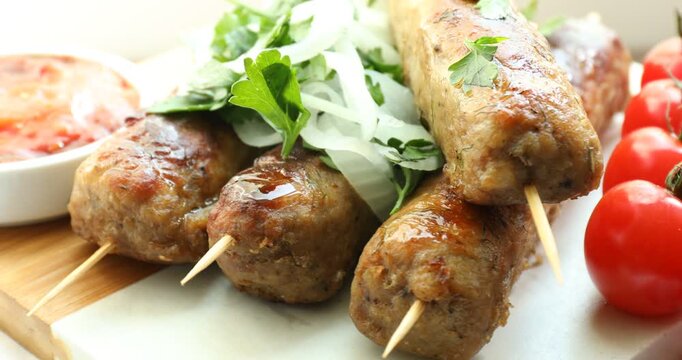 Tasty kebabs with spices, tomatoes and sauce on board, closeup