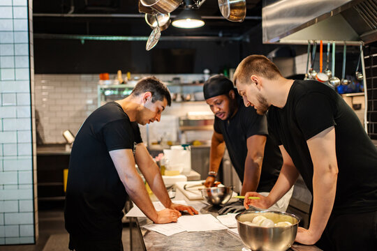 Three chefs in a commercial kitchen collaborating and discussing menu items