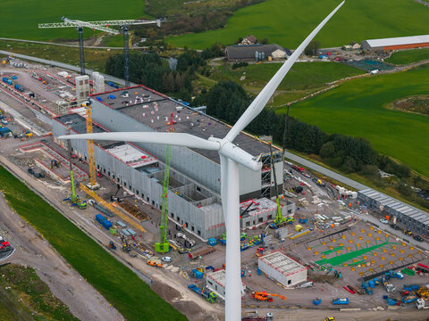 Aerial view of the Green Mountain data center construction site in Undheim, featuring a large wind turbine, cranes, and industrial equipment set against green fields in Rogaland, Norway.
