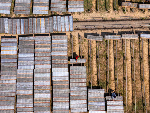 Aerial view of workers tending to rows of rectangular drying racks on dry soil in Polanharjo, Central Java, Indonesia.