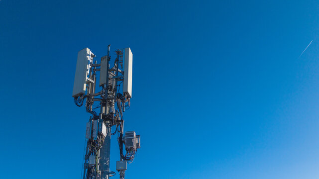 Aerial view of a phone mast with communication equipment and cables against a clear blue sky in Camberley, England, United Kingdom.