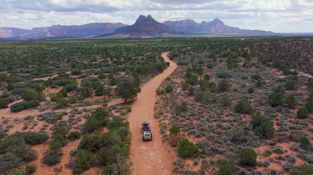 Aerial view of SUV towing a teardrop camper trailer overland on a dirt road on Gooseberry Mesa while Zion National Park mountains rise in the background.