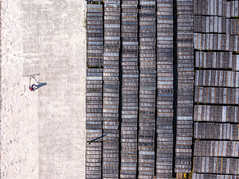 Aerial view of a worker raking material on a large light-colored surface next to rows of dark rectangular frames in Polanharjo, Central Java, Indonesia.