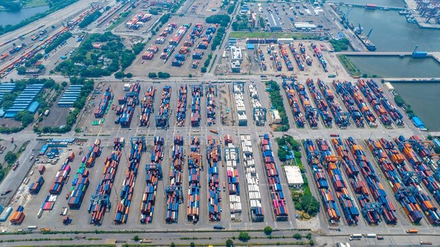 Aerial view of Jawaharlal Nehru Port Authority with rows of colorful shipping containers, industrial cranes, and logistics infrastructure in Juna Sheva, Maharashtra, India.