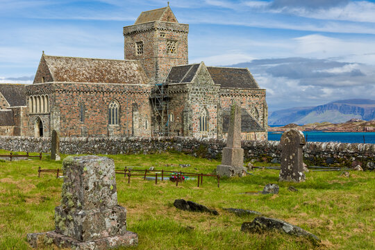 Historic stone abbey with ancient headstones in graveyard, Isle of Iona, Inner Hebrides, sea and coastal mountains in distance