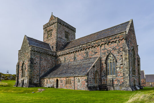 Historic stone abbey building on Isle of Iona, Scotland, showing medieval pink granite masonry, slate roof and central tower above green lawn