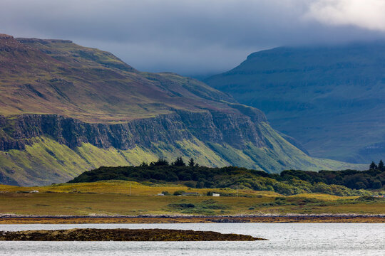 Grassy coastal hillsides and jagged cliffs dropping down to sea, low clouds drifting across mountain tops in moody weather
