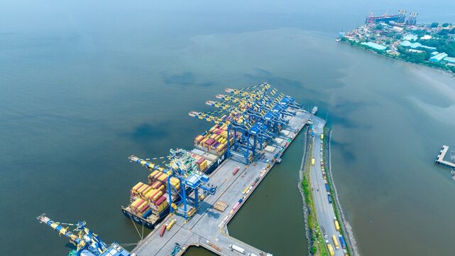 Aerial view of Jawaharlal Nehru Port Authority with a container ship, gantry cranes, and shipping containers at the terminal in Juna Sheva, Maharashtra, India.