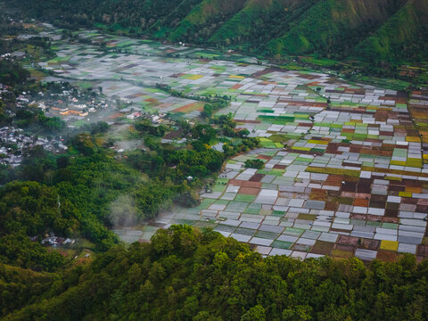 Aerial view of the Sembalun agricultural basin nestled at the foothills of Mount Rinjani with vibrant patchwork fields and lush green slopes in Sembalun, West Nusa Tenggara, Indonesia.