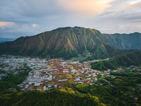 Aerial view of the Sembalun agricultural basin nestled at the foothills of Mount Rinjani with patchwork fields and lush green slopes in Sembalun, West Nusa Tenggara, Indonesia.