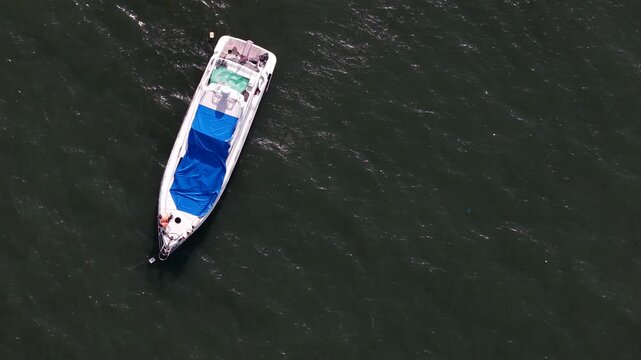 A motorboat covered by a blue tarp floats on dark green water, evoking a sense of tranquility, relaxation, and nautical travel, while reflecting a minimalist coastal lifestyle aesthetic