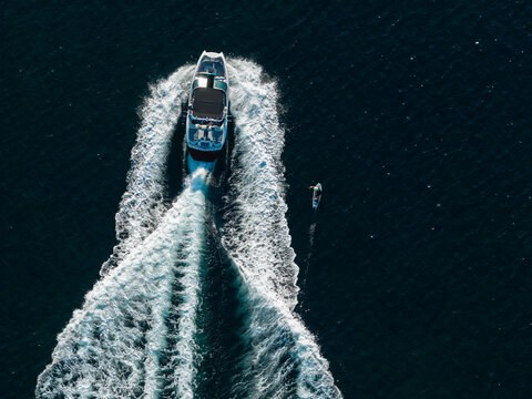 Aerial view of a motorboat pulling a person on a wakeboard, creating a white wake on the deep blue Mediterranean Sea in Antibes, Provence-Alpes-Cote d'Azur, France.