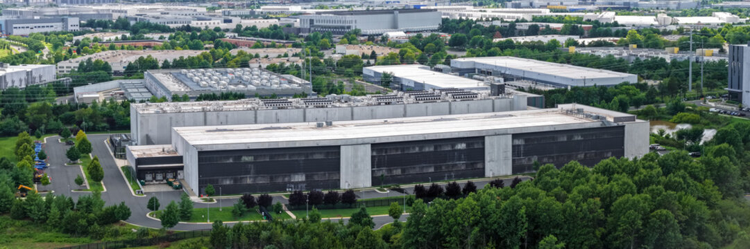 Aerial view of a large data center building with rooftop cooling units, surrounded by parking lots and dense green trees in an industrial park in Ashburn, Virginia, United States.