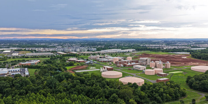Aerial view of a water treatment facility with large circular storage tanks and industrial buildings surrounded by lush green forests and suburban development in Ashburn, Virginia, United States.