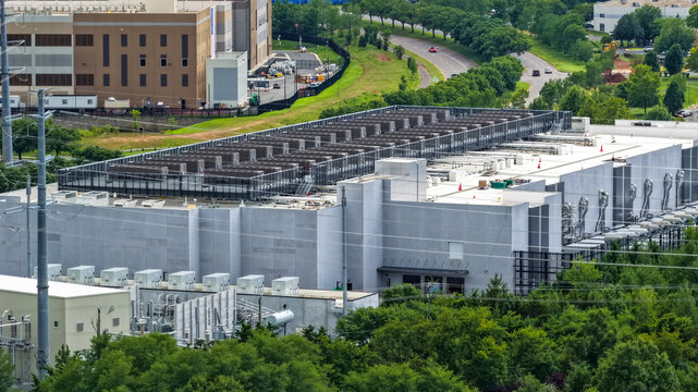 Aerial view of a large data center facility with rooftop cooling units and industrial infrastructure surrounded by trees and a road in Ashburn, Virginia, United States.