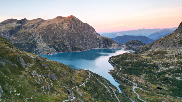 Aerial view of Barrage d'Emosson, a large dam creating a reservoir with turquoise water, surrounded by rugged alpine mountains and winding roads in Finhaut, Valais, Switzerland.