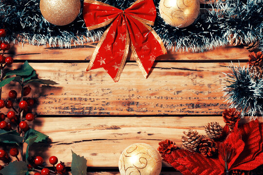 Christmas background with a frame, gold ornaments, a red bow, and decorative pine cones on rustic wood, with space for text.