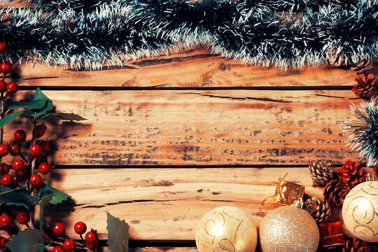 Framed Christmas background on a rustic wooden table, decorated with tinsel, gold ornaments, and pinecones, with space for text.