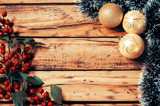Christmas background adorned with gold ornaments and decorative tinsel, green leaves on rustic wood, with ample space for text.