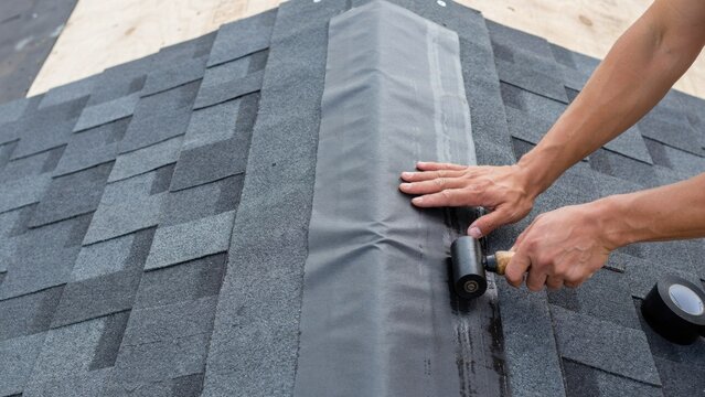 Workman installing new black underlayment on a freshly shingled roof for enhanced water barrier protection.