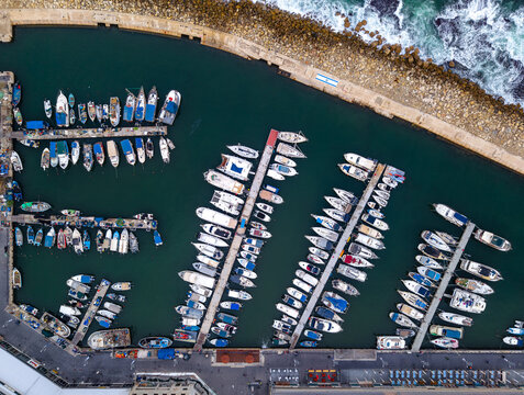 Aerial view of the Old port of Jaffa with numerous boats moored in the marina, calm turquoise water, and stone breakwaters in Tel Aviv-Yafo, Tel Aviv District, Israel.