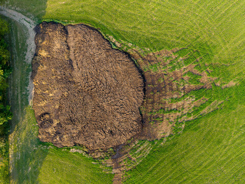 Aerial view of a large pile of manure in a green agricultural field with visible dirt tracks in Czechia.