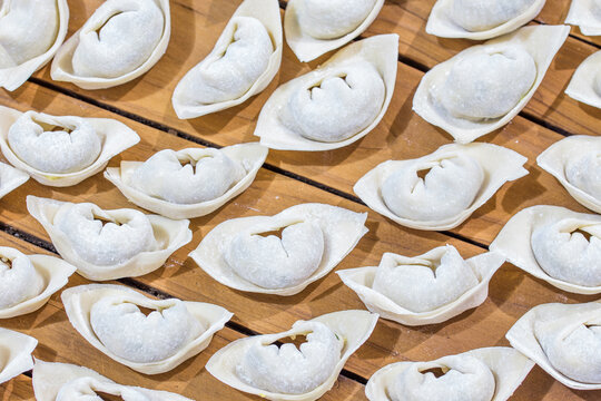 Uncooked handmade dumplings neatly arranged on a slatted wooden surface, prepared for cooking.