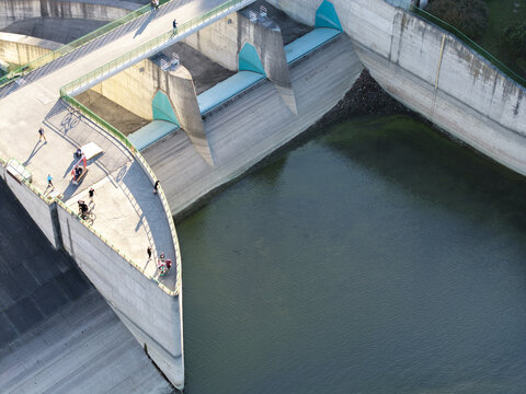 Aerial view of Niedzica Dam with people walking along the concrete structure and green railings overlooking the water reservoir in Niedzica, Malopolskie, Poland.