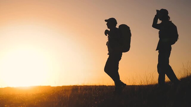 Business team silhouette hill. Two hikers stand silhouetted against a sunset, with backpacks, as the bright sun sets. The two men, enjoying the view, seem reflective in the golden hour.