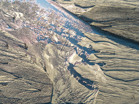 Aerial view of intricate sand patterns and a water channel flowing through a coastal landscape in Poland.