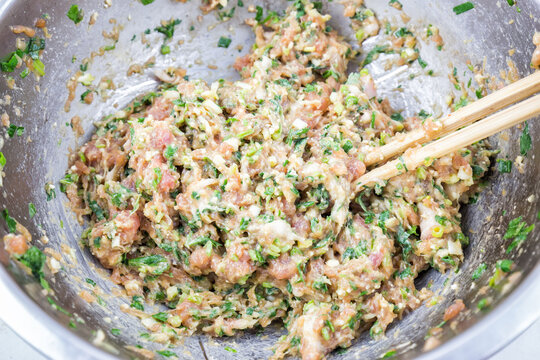 Raw savory minced meat filling mixed with fresh green herbs, prepared in a metal mixing bowl with chopsticks for cooking use.