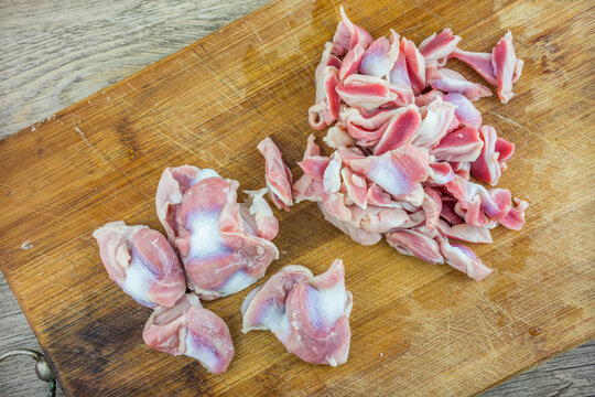 Raw sliced chicken gizzards, whole and cut, placed on a wooden cutting board for food preparation.