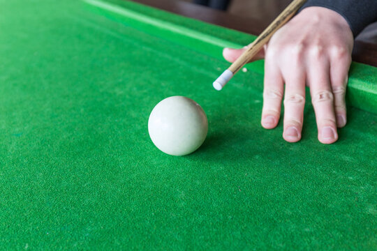 A close-up view of a person's hand and pool cue preparing to strike the white cue ball on a green felt billiards table.