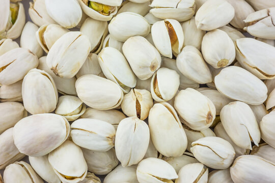 A dense collection of whole pistachios, some in open shells revealing kernels, others closed, showcasing their natural texture and appearance.
