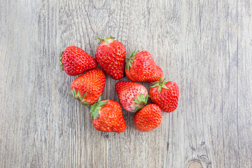 Several fresh ripe red strawberries placed on a light textured wooden surface, viewed from top. © tai