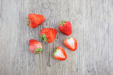 Whole and sliced ripe red strawberries arranged on a textured light wooden surface. © tai