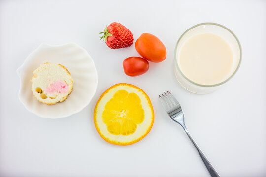 A variety of breakfast items including milk, fruits, cake, and utensils arranged on a white surface.